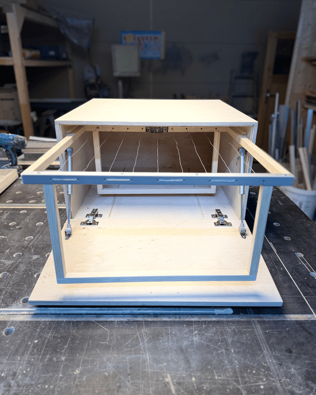 DryBox, a drying box for herbs opened up. A wooden frame with metal brackets on a workshop floor