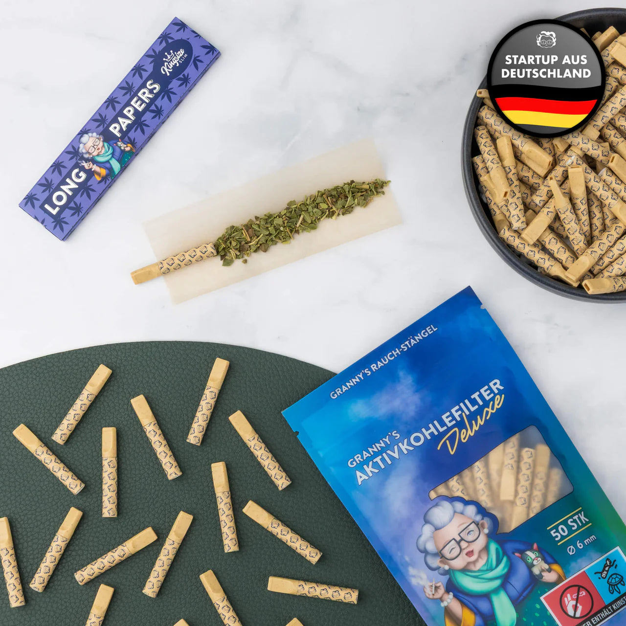 Cannabis products including papers, rolling paper with herbs, and activated carbon filters on a white surface.