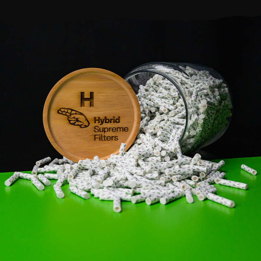 A clear jar with Hybrid Supreme Filters spilling out onto a green surface, with a wooden lid featuring the brand's logo.