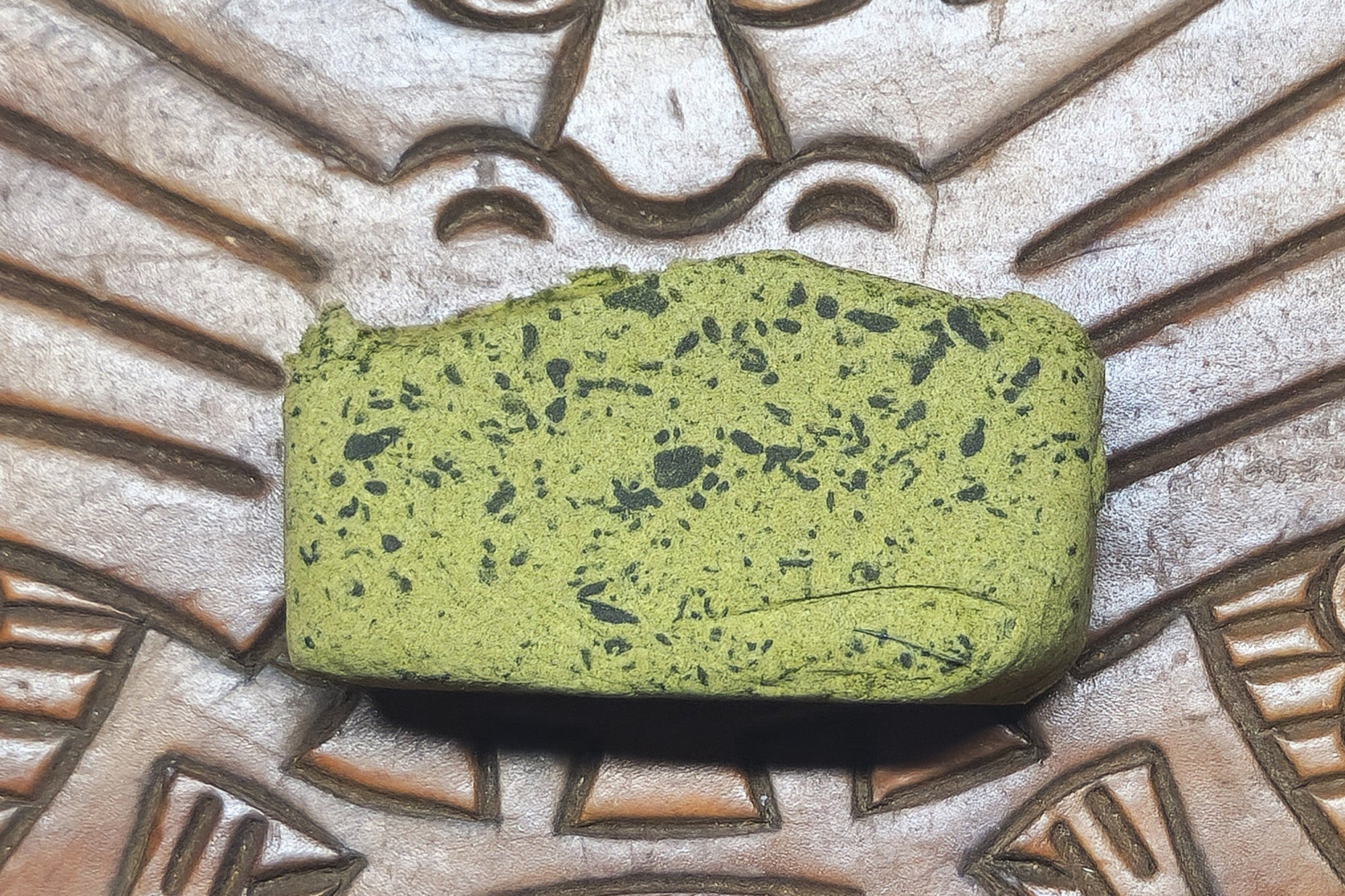 Green pollen with black specks on a textured surface with patterns
